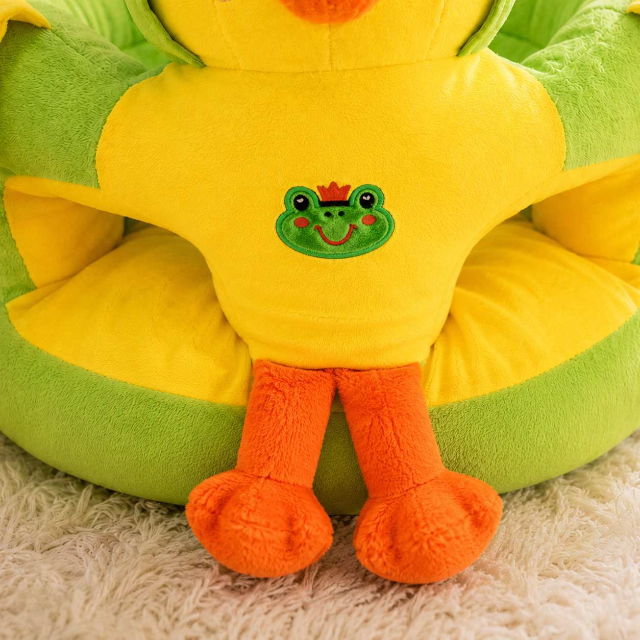 Plush toy frog with a green face and orange feet on a green and yellow cushion.
